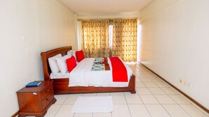 A hotel room with a wooden bed, white bedding, red pillows, a wooden nightstand, and a white rug.