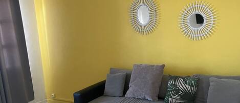 A living room with a yellow wall, a dark blue sectional sofa, a white coffee table, and two wall-mounted decorative items.