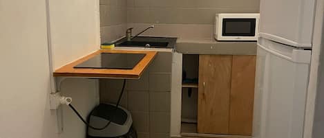 A compact kitchen with a microwave, a refrigerator, and wooden cabinets.