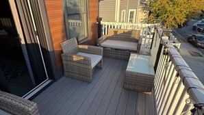 Een terras met rieten meubilair, een glazen deur en een witte picket hek.