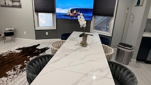 Een moderne woonkamer met een grote witte marmeren tafel, twee zwarte fauteuils, een wandgemonteerde televisie en een decoratieve orchidee vaas.