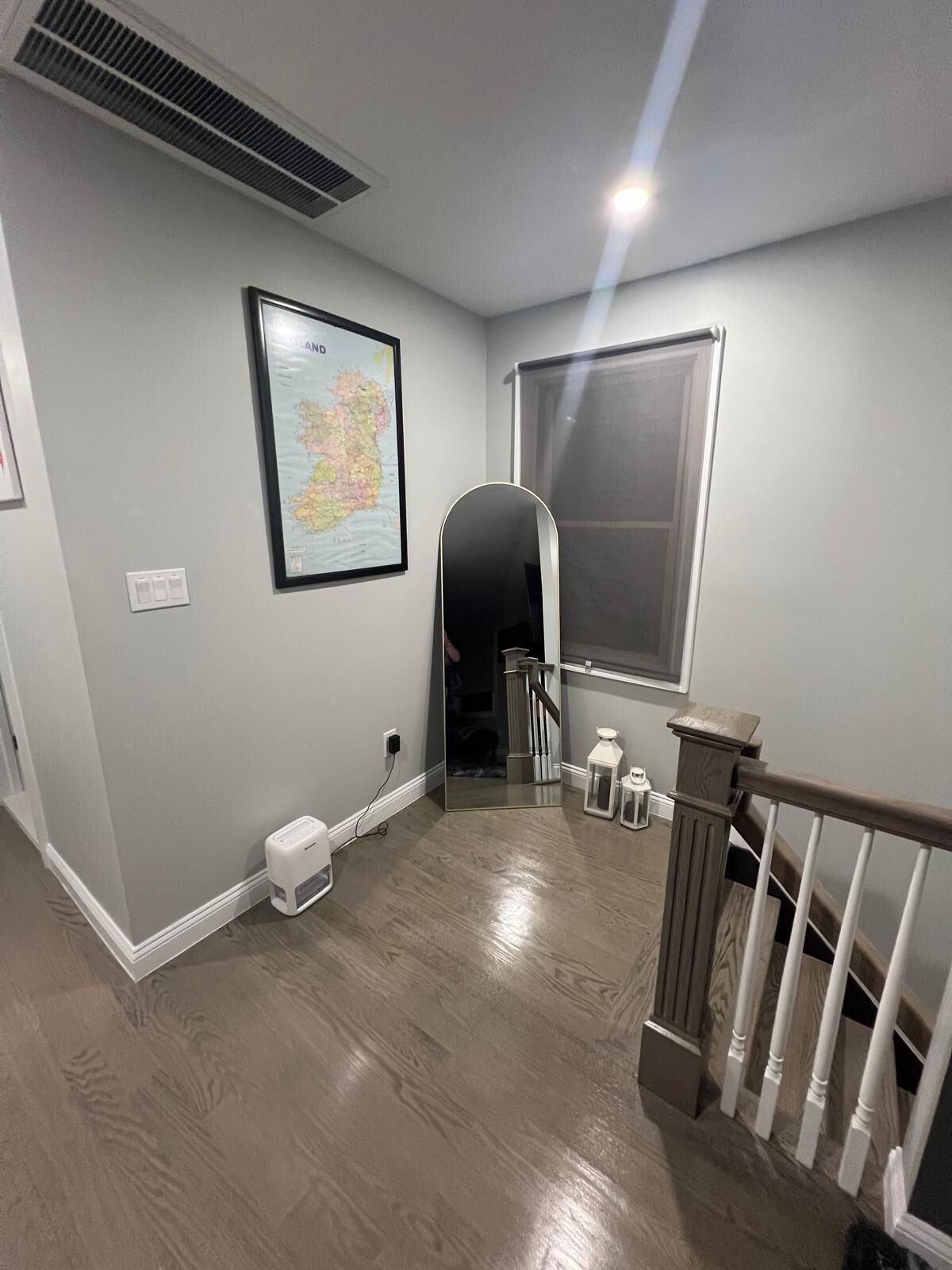 Un couloir avec une carte encadrée, une fenêtre, un miroir et un escalier.