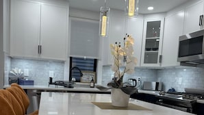 Een moderne keuken met witte kasten, een centraal eiland, hanglampen en een decoratieve orchidee-arrangement.
