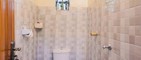 A small bathroom with a toilet, a shower, and a window above the toilet.