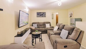 Un salon comprenant un canapé, une petite table avec une plante et un téléviseur fixé au mur.