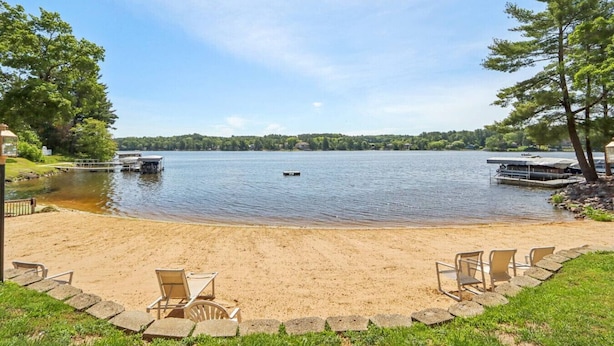 Une propriété au bord du lac, dotée d’une plage de sable, d’un quai et d’une rangée de chaises.