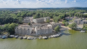 Un hôtel situé au bord de l’eau, composé de plusieurs bâtiments, avec un quai où sont amarrés des bateaux et entouré d’une zone boisée.