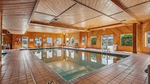 Une grande piscine intérieure aux murs et au plafond en bois, entourée d’un sol carrelé et dotée de plusieurs points d’accès.