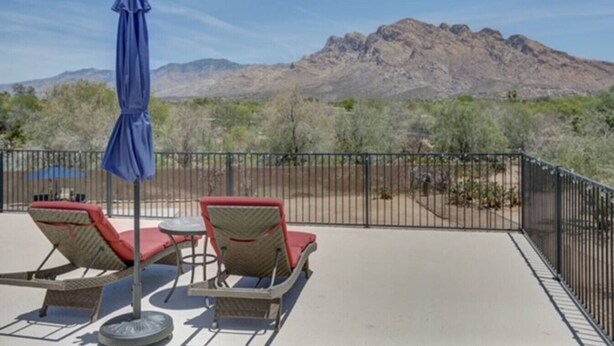 Un patio con dos sillas de mimbre y una mesa, una sombrilla azul y vistas a una cordillera.