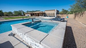 Una piscina rectangular con borde de piedra, rodeada de sillones de descanso y una zona de terraza cubierta.