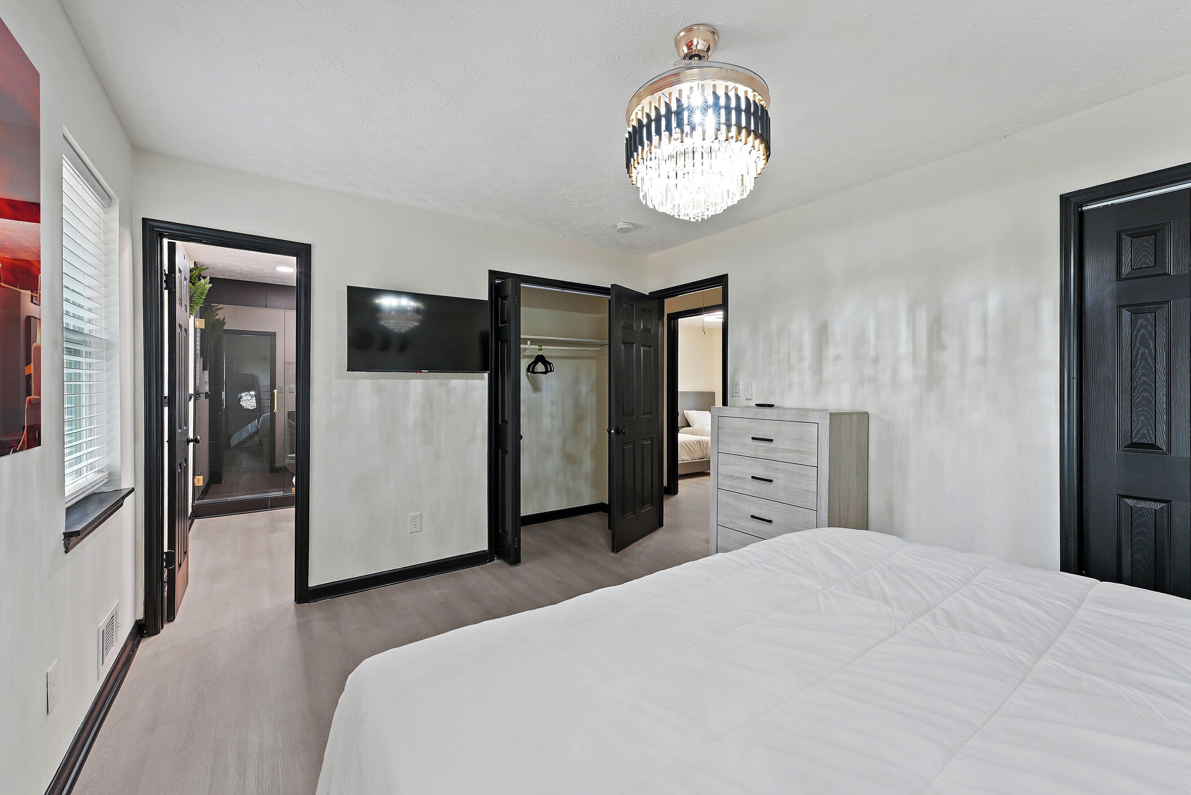 Une chambre à coucher avec un lit, une commode, un téléviseur et un lustre.