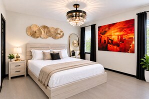 A modern bedroom with a large bed, a chandelier, a wall art piece, and a bedside table with a lamp.