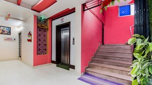 Eine Treppe mit roter Wand, einer Aufzugtür, einem Feuerlöscher und einem Deckenventilator.