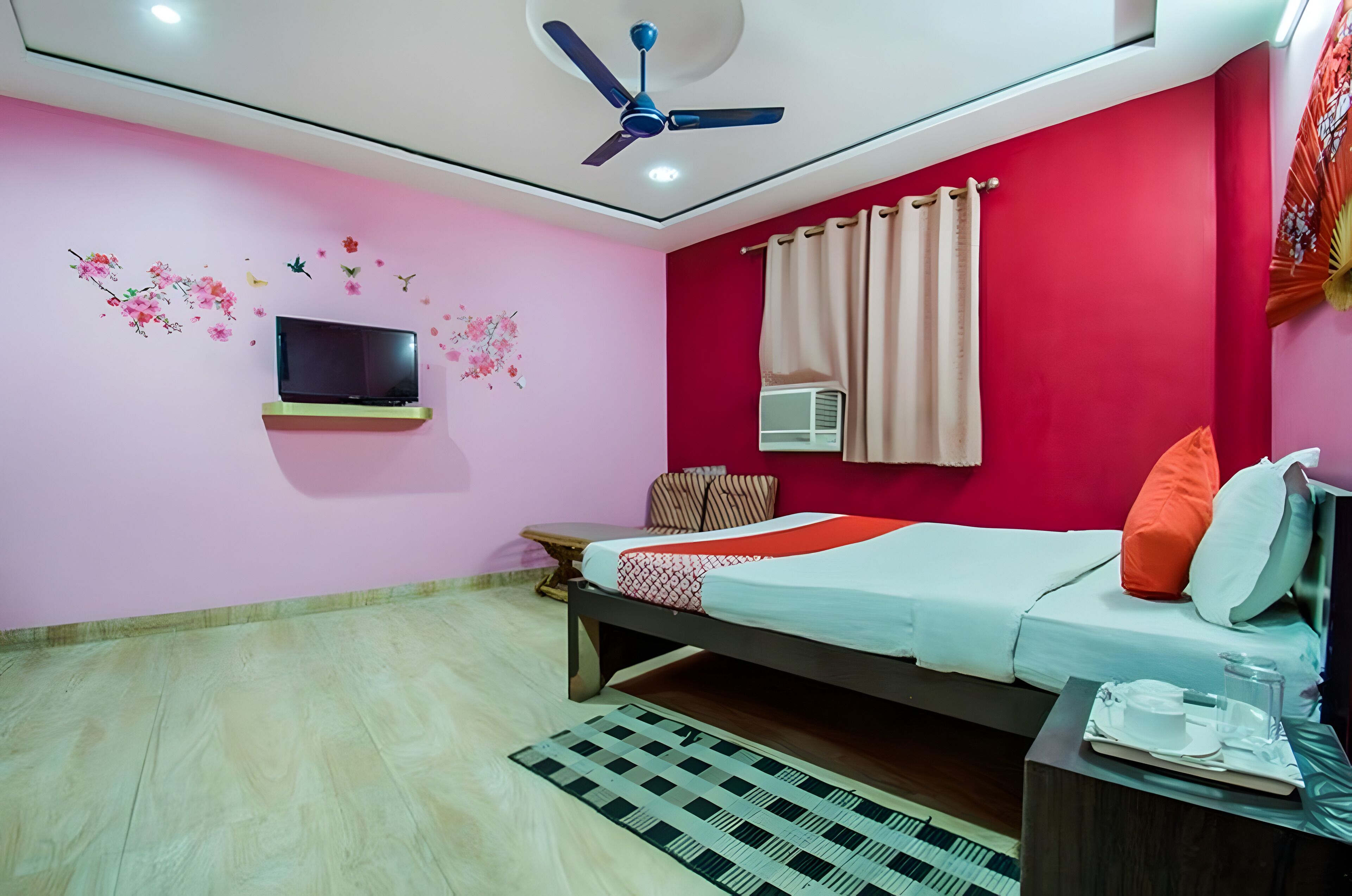 Un dormitorio con cama, televisor, ventilador de techo y ventana con cortinas.