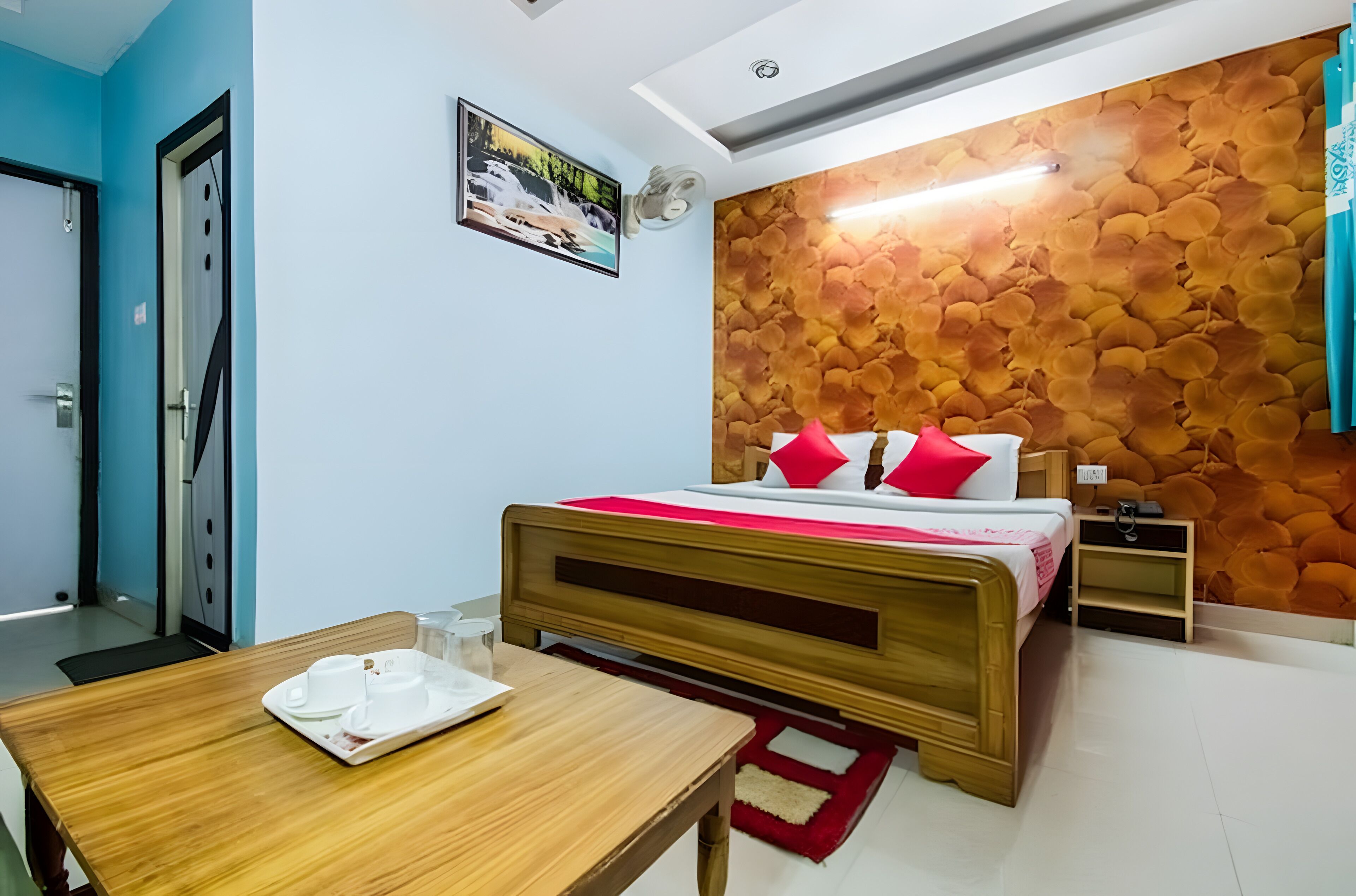 A bedroom with a wooden bed, a nightstand, a wall-mounted light, and a dining table with a tray of white cups.