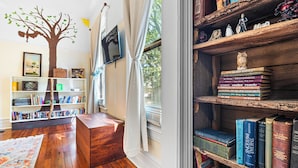 Ein gemütliches Zimmer mit Holzboden, einem Bücherregal, einem Schreibtisch und einem Fenster mit Vorhängen.