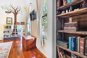A cozy room with a wooden floor, a bookshelf, a desk, and a window with curtains.