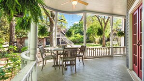 Eine überdachte Veranda mit Tisch und Stühlen, einem Deckenventilator und Blick auf ein Haus und Bäume.