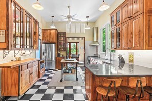A kitchen with wooden cabinets, a black and white checkered floor, a ceiling fan, and a large island with stools.