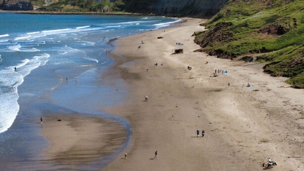 Ein weiter Strand mit Klippen an einer Seite und dem Meer auf der anderen.
