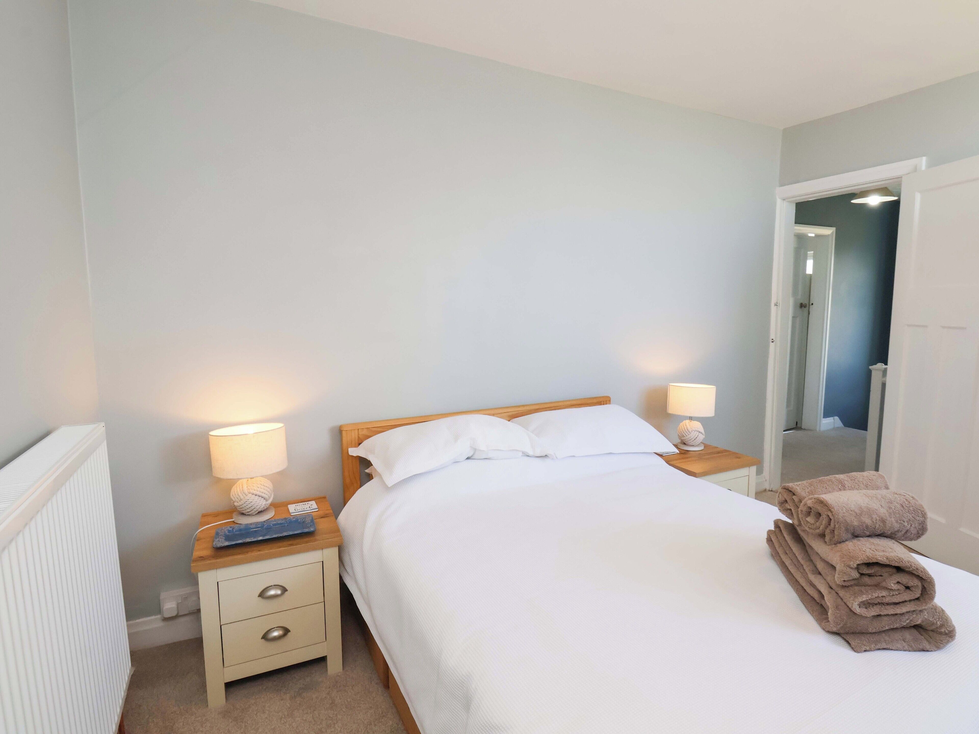 A neatly made bed with white linens, two bedside tables with lamps, and a stack of folded towels.