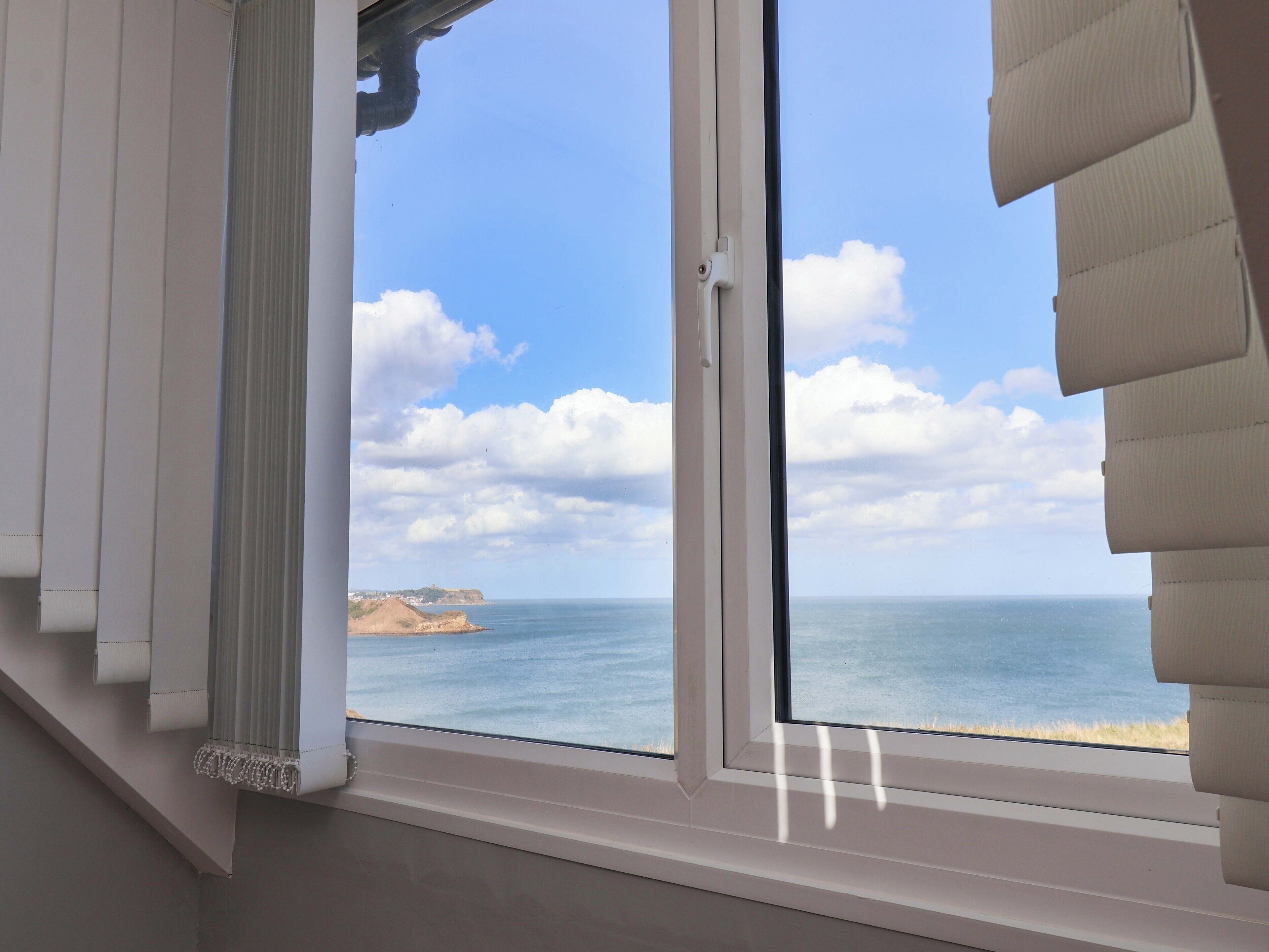 A room with a large window overlooking a coastal view, including a sandy beach and cliffs.