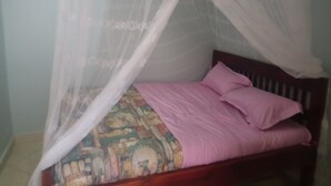 Una cama con cabecera de madera, colchón estampado y manta rosa.