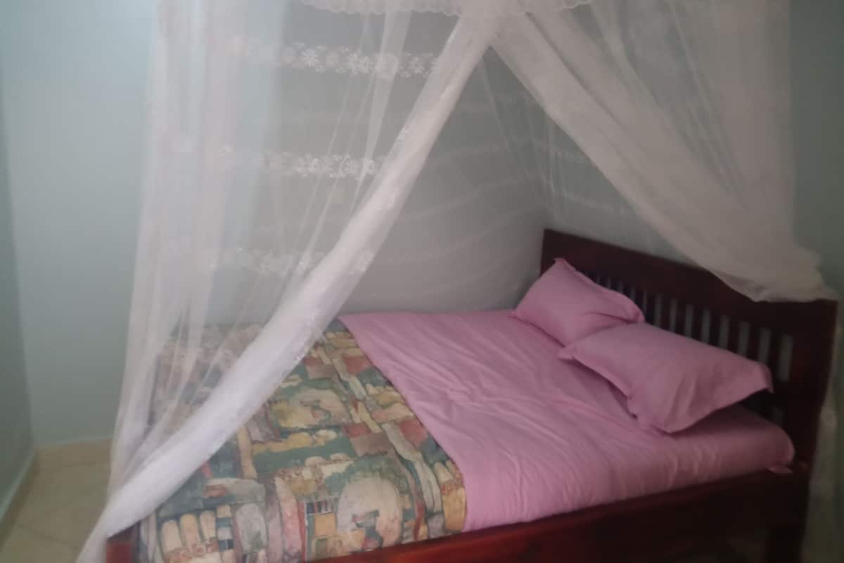 Ein Bett mit Holz-Kopfteil, einer gemusterten Matratze und einer rosa Decke.