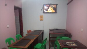 Una habitación pequeña con dos escritorios de madera, sillas de plástico verde, un televisor montado en la pared y un letrero que indica pago con móvil.