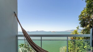A hammock on a balcony with a view of a calm body of water and distant mountains.
