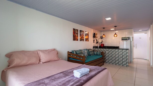 A bedroom with a large bed, a sofa, and a kitchenette in the background.