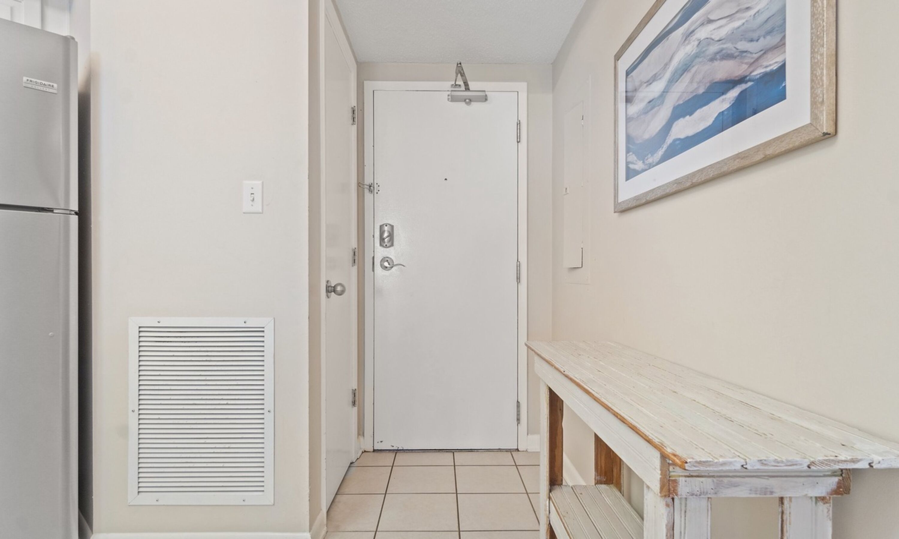 A narrow hallway with a white door, a vent on the left, and a wooden bench on the right.