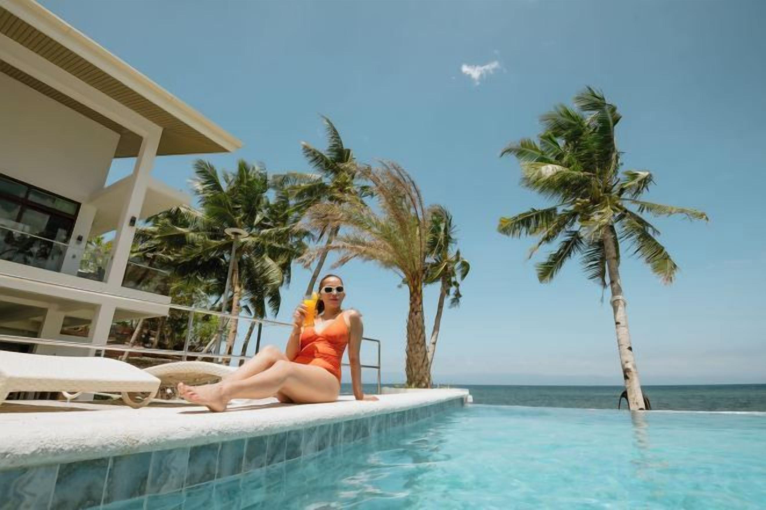 A person sitting by a pool with a view of the ocean and palm trees.