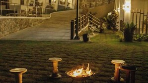 A nighttime outdoor area with a fire feature, a staircase, and a building with multiple windows and lights.
