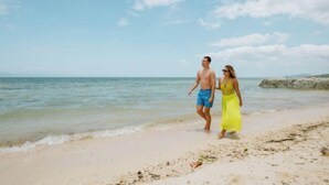 A couple walking on a beach with clear skies and calm water.