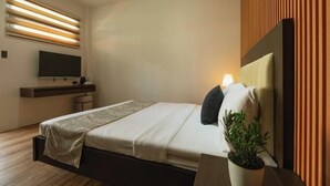 A modern bedroom with a bed, bedside table, TV, and a potted plant.