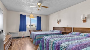 Une chambre d’hôtel avec deux lits, un ventilateur de plafond, une fenêtre avec des rideaux, un bureau en bois et un radiateur.