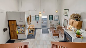 Un hall d’hôtel avec un escalier en bois, un comptoir d’accueil, un espace salon et une cuisine dotée d’une cheminée.