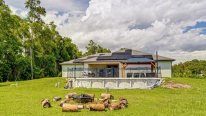 Ein modernes Haus mit Solaranlage, einem Swimmingpool und einem Rasen mit Holzstämmen.