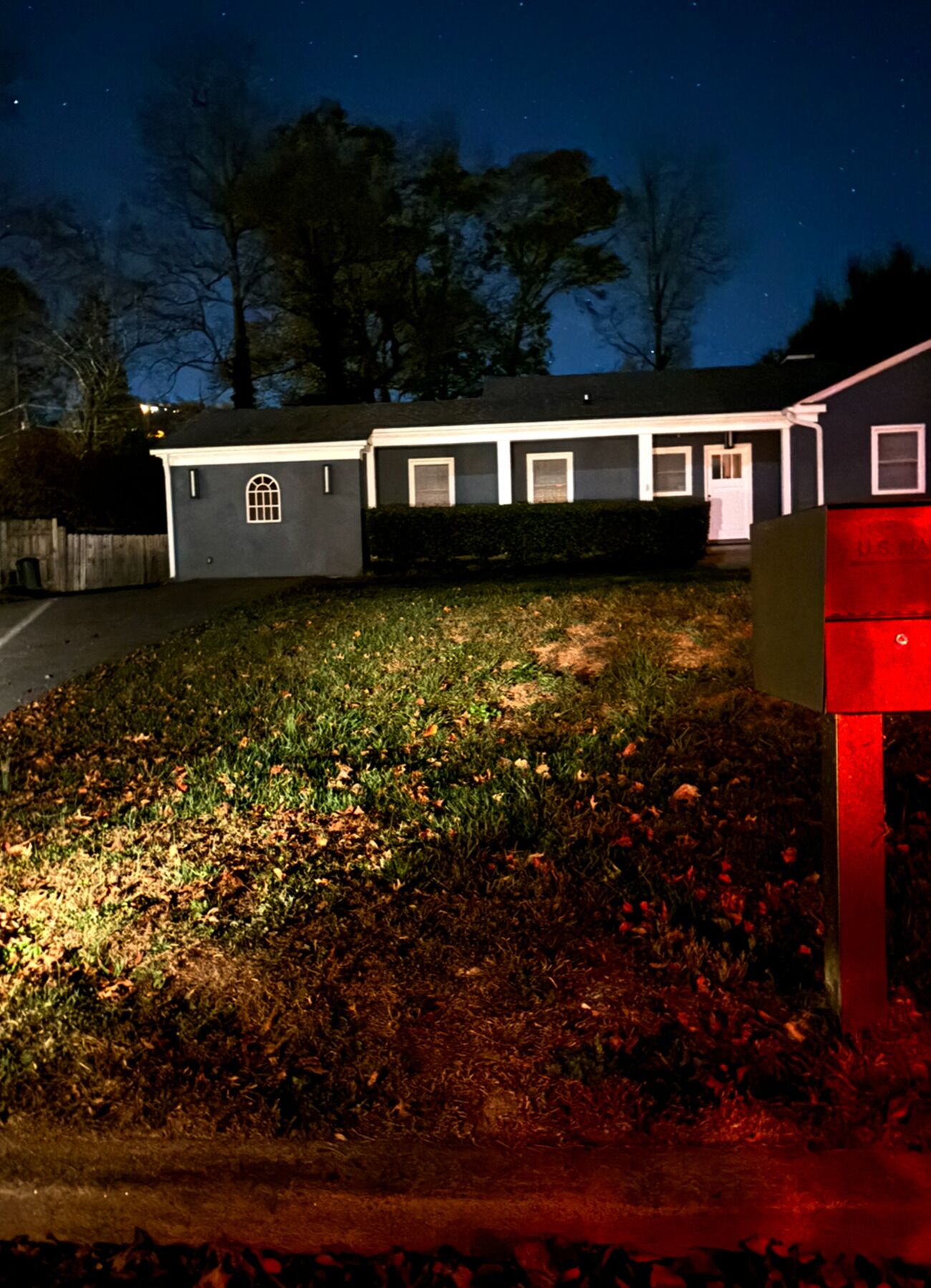 Ein Wohnhaus bei Nacht mit einer gut beleuchteten Rasenfläche und einer Garage.