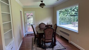 A dining area with a table and chairs, a ceiling fan, and a window with a view of greenery.