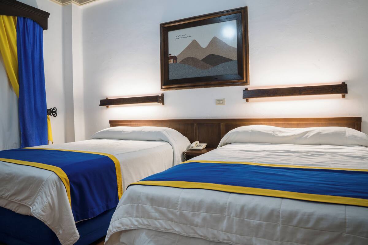 A hotel room with two beds, each with a blue and yellow bedspread, a framed picture on the wall, and a telephone on the nightstand.