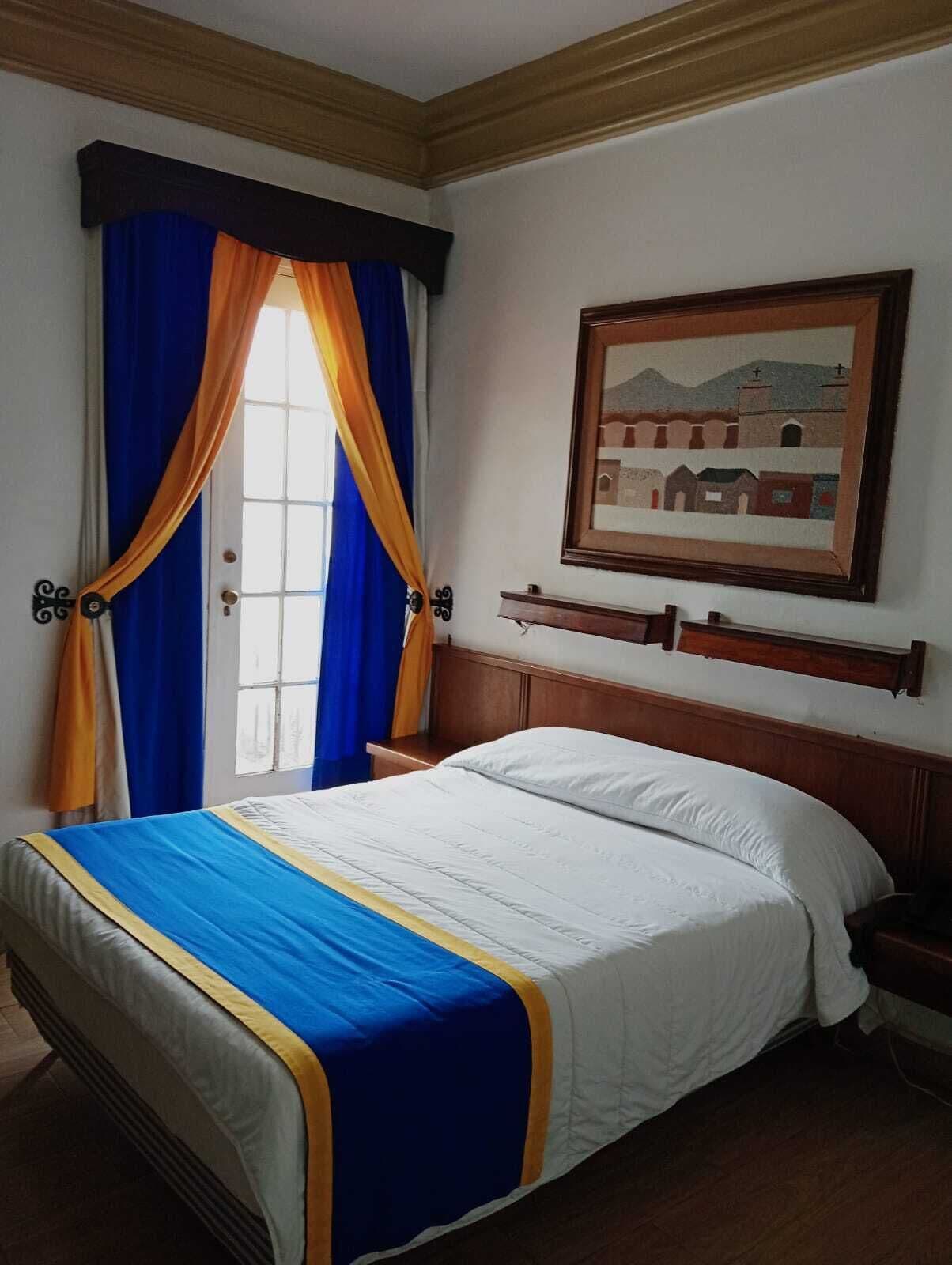 A bedroom with a bed, curtains, a painting, and a nightstand.