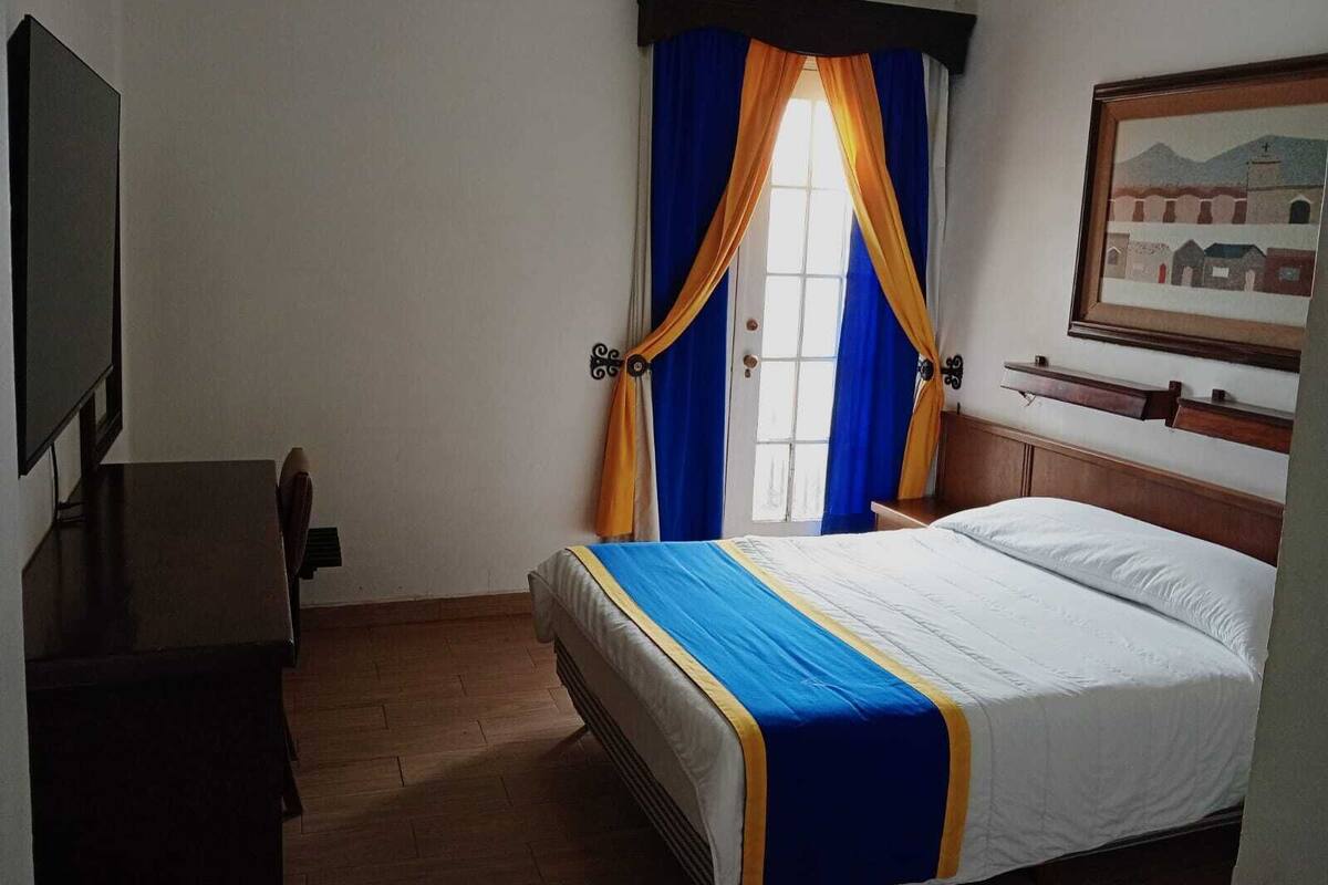 A hotel room with a bed, a desk, a television, and a window with curtains.