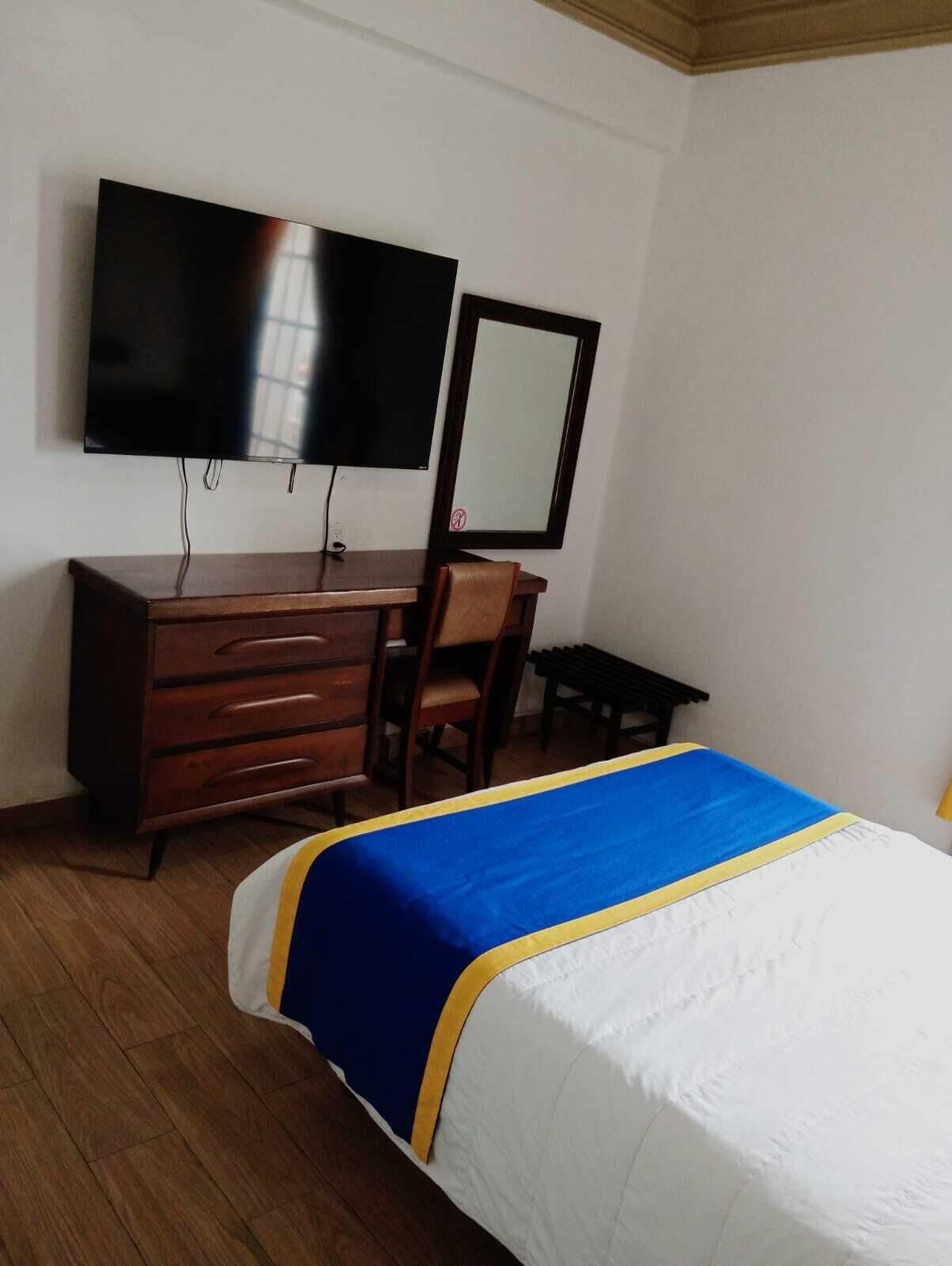 A hotel room with a bed, a wooden dresser, a television, and a mirror.