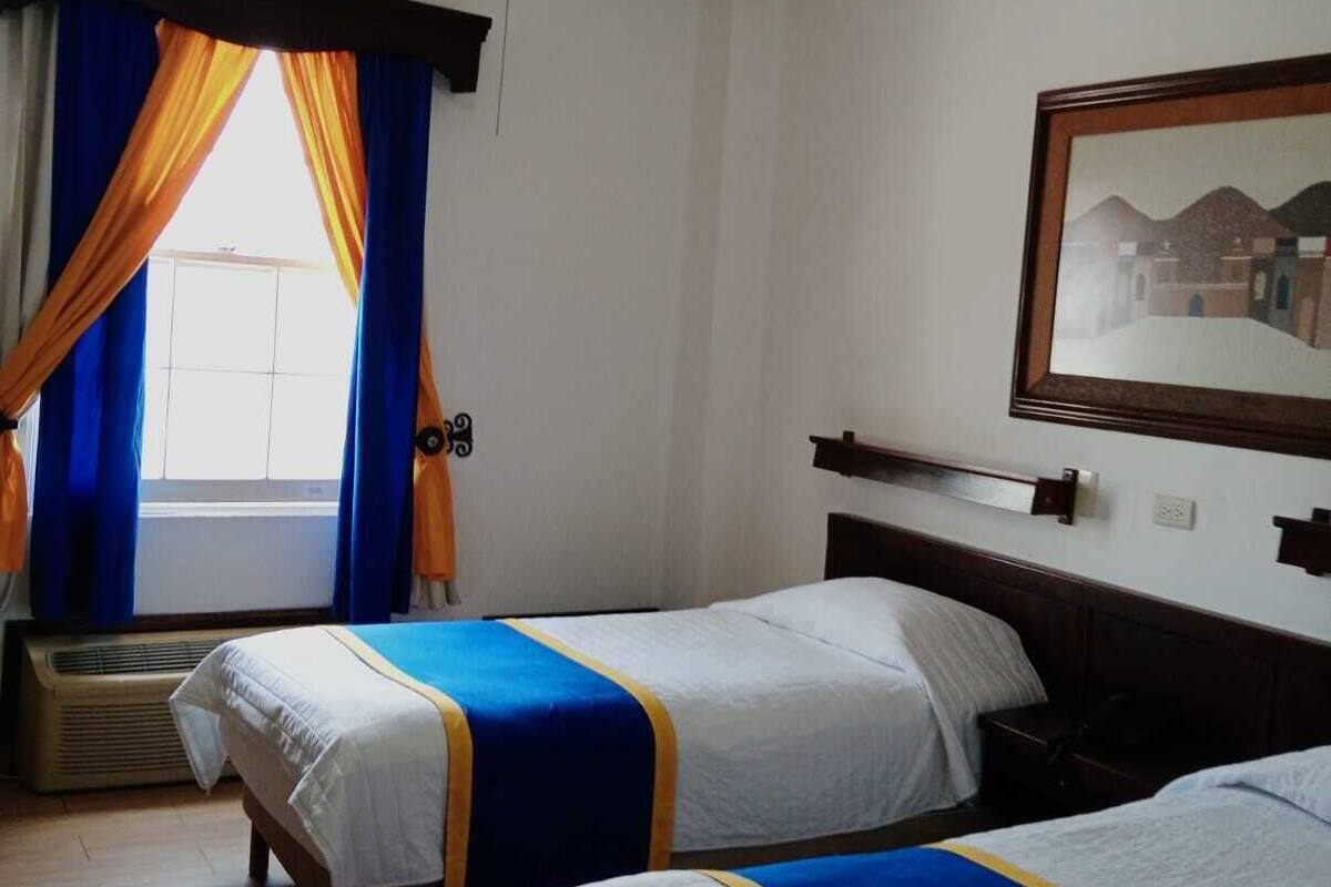 A hotel room with two beds, a ceiling fan, a window with curtains, and a framed picture on the wall.