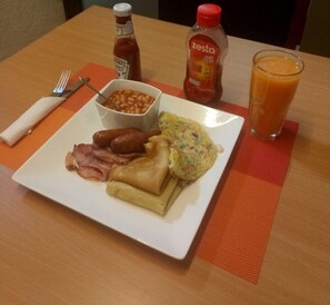 Ein Teller Frühstück mit Eiern, Speck, Würstchen, Bohnen, Toast und zwei Flaschen Ketchup und Senf.