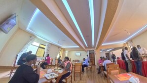 A dining area with tables and chairs, a television mounted on the wall, and a group of people standing and conversing. - Kiandani Hotel Machakos (Machakos)