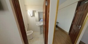 Ein schmaler Flur, der zu einem Badezimmer mit Toilette, Waschbecken und Spiegel führt.