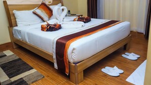 A neatly made bed with a wooden frame, white linens, and a brown throw blanket. There are slippers on the floor and a small rug beside the bed. - Kiandani Hotel Machakos (Machakos)